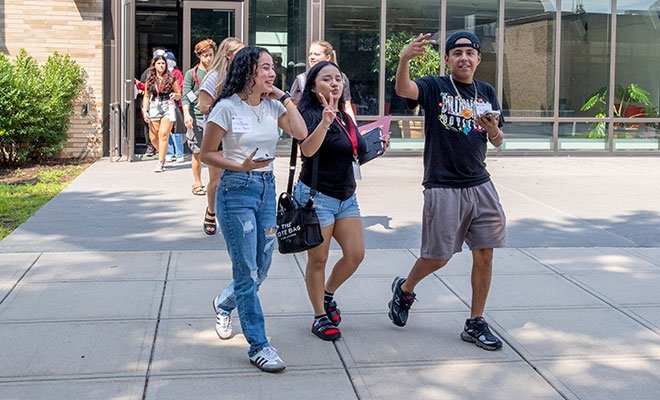 Young students walking happily in sunshine on campus, smiling at camera