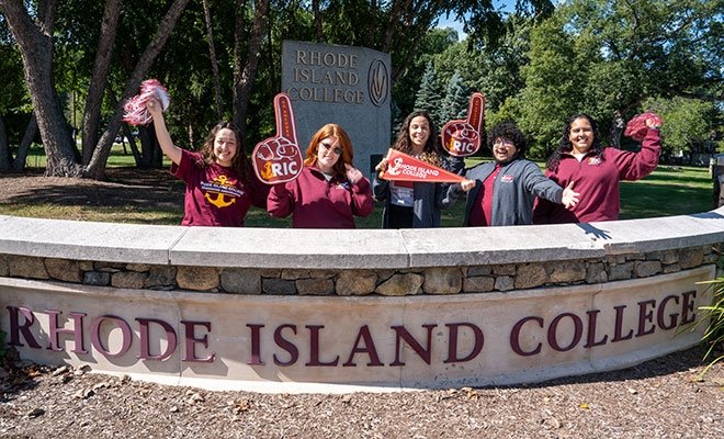 Admissions team excited at RIC entrance in RIC gear and holding foam fingers, pennants, pom poms