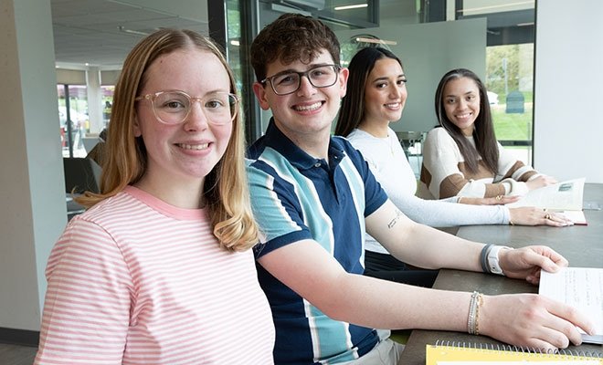Four smiling students in sunny building lobby