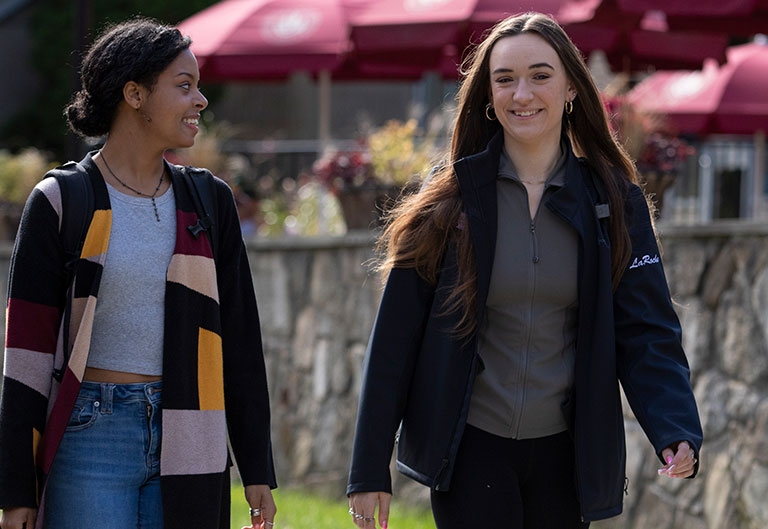 Students cheerfully walking near dining center's outdoor umbrella seating area