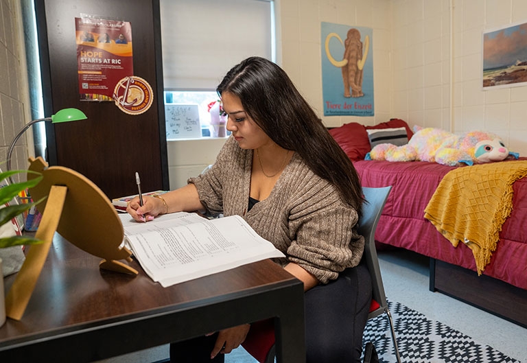 Student writing at desk in dorm room