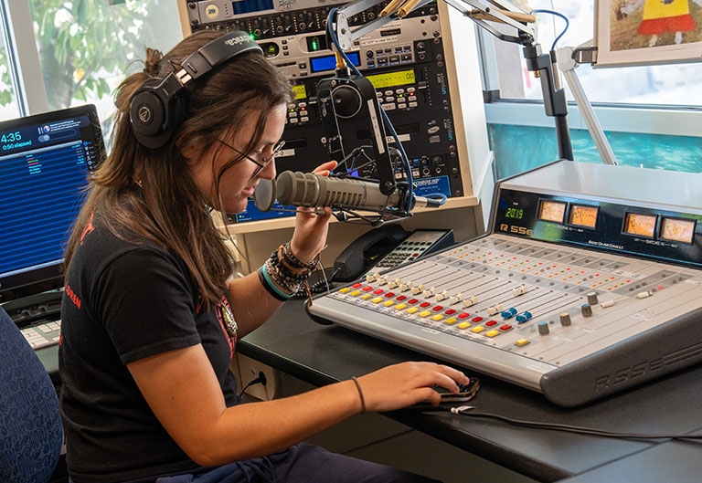 Person working at sound board with microphone and headphones on