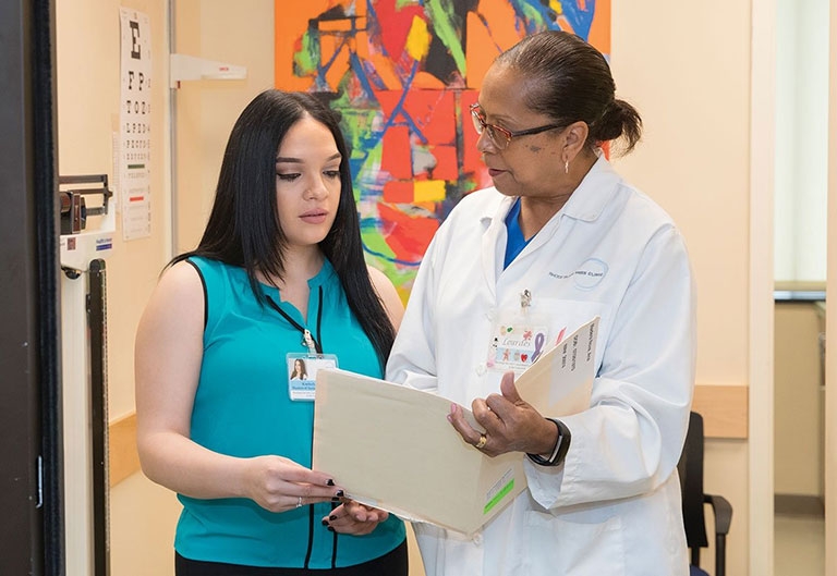 Person in lab coat speaking with student as they look at a medical chart