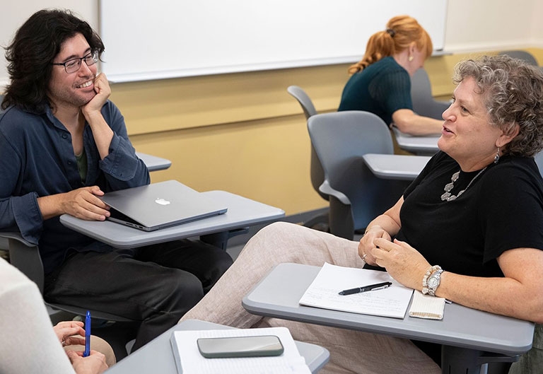 Faculty at desks, talking happily, with laptops, notebooks and pens