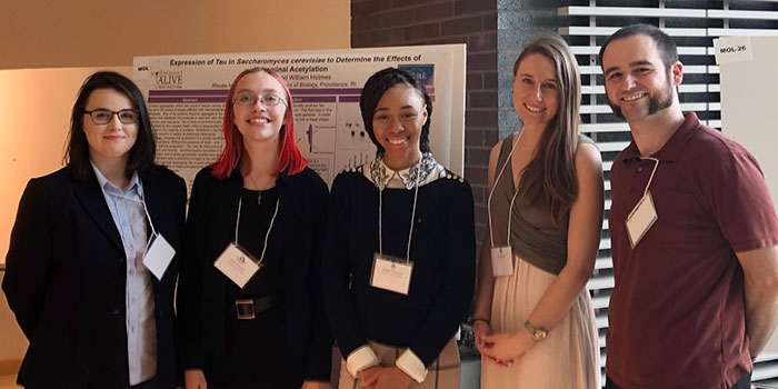 Holmes’ student researchers pose in front of their poster at the 2018 SURF Conference at URI, where they presented their research. From left, Ali Griffith, Jess Anderson, Abigail Fleurima, Anna (Lally) Bock ’18 and RIC Assistant Professor of Biology Bill Holmes.​