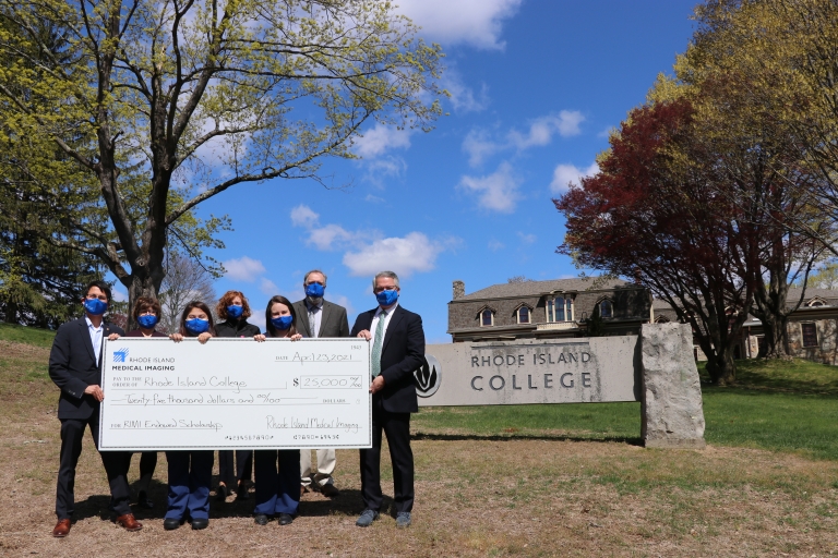 The leadership of RI Medical Imaging presents President Sanchez with a check for a scholarship fund in front of the Rhode Island College sign at the Forman Center