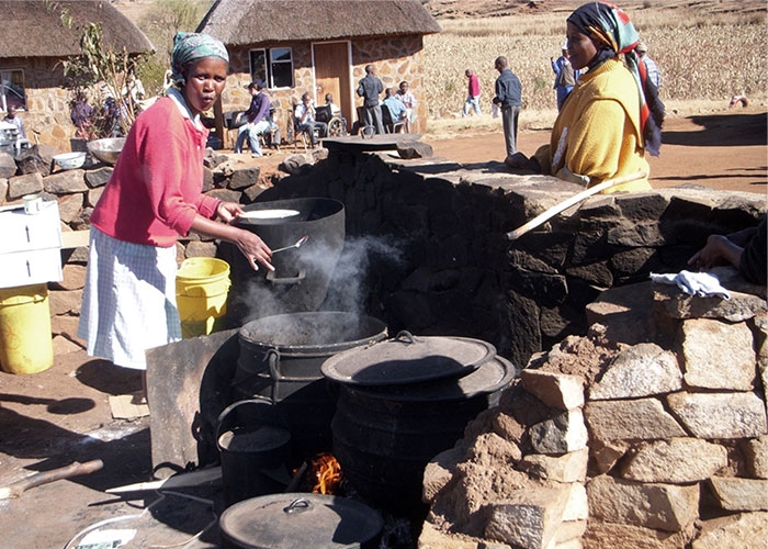 Two women cooking children's lunch over huge black cauldrons
