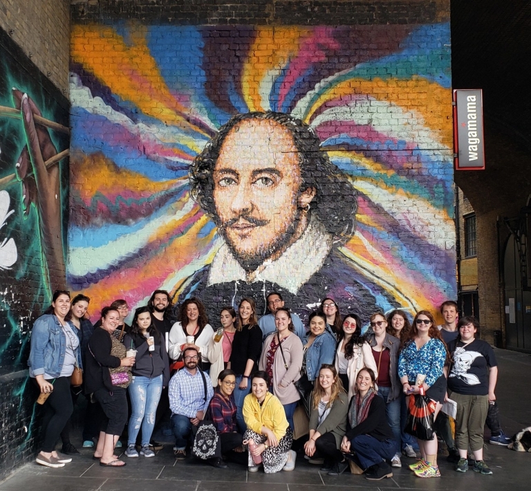 Class in London standing in front of portrait of Shakespeare