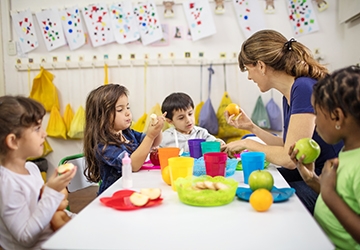 Teacher sitting with students at table holding, discussing fruit