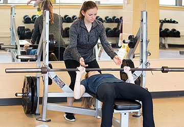 Student spotting another student lifting weights at rec center