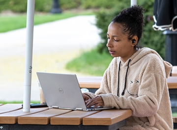 Student working on laptop at picnic table on campus