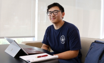 Hope Scholar Tytain Sun in Cybersecurity Camp t-shirt at desk with computer, notebook, and pen