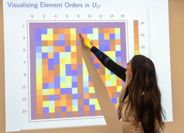 Student points to a vibrant projected presentation in a math class