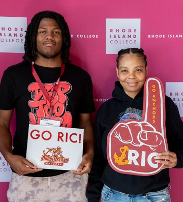 Mother and son holding a go RIC sign and a RIC foam finger at orientation