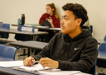 Accounting student sits, attentive in class with pen and paper