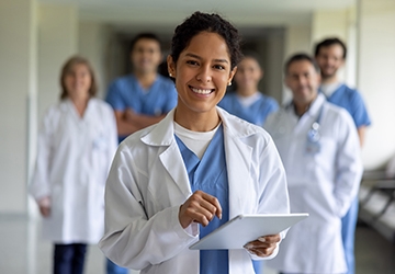 Medical professional with clipboard with several other medical professionals in the background
