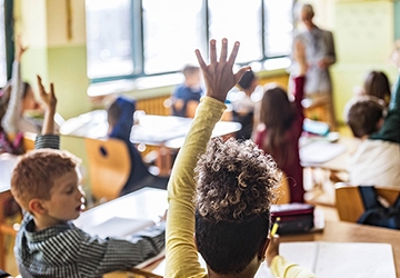 Young students raising their hands in class