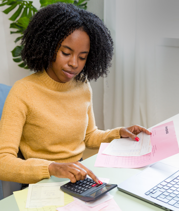 Female, black accountant working at desk with invoices, calculator, and laptop