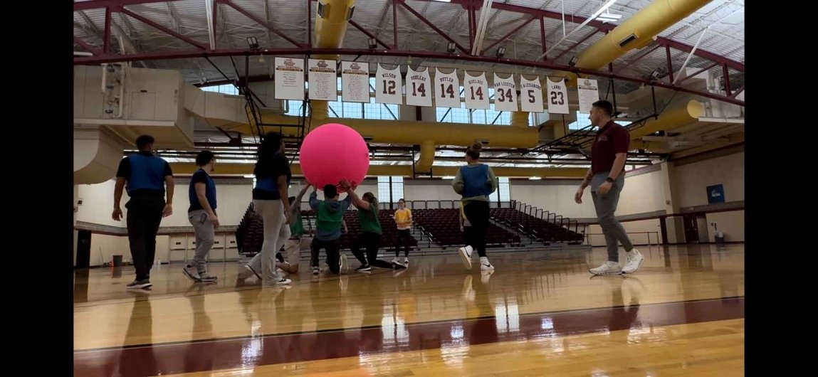 HPE students in gym utilizing engaged learning with giant ball