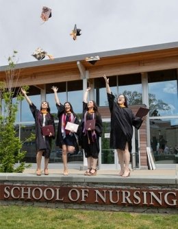 Nursing students, in front of the school of nursing, dressing in caps and gowns, throwing their caps in the air