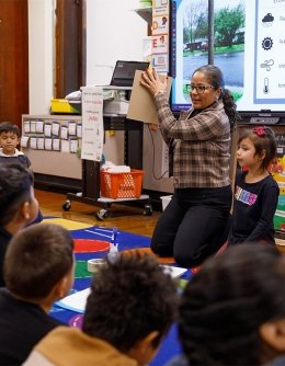 A teacher apprentice working with young children on a classroom rug