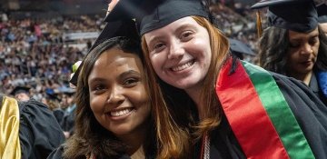 Two happy graduates posing together at commencement ceremony