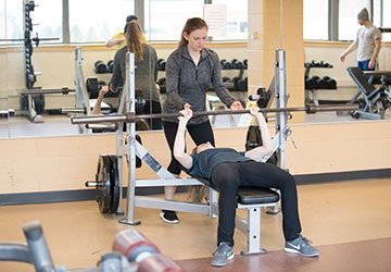 Woman in gym spots person doing a bench press