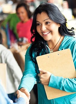 Latina woman holding clipboard, shaking someone's hand in a crowd