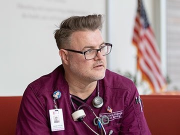 Nursing student David Fields in scrubs with badge, stethoscope, american flag in background