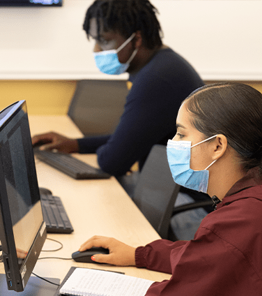 Two students with masks on computers 