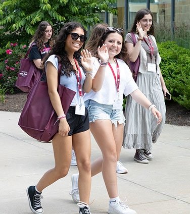 Students smiling, while waving and walking on campus