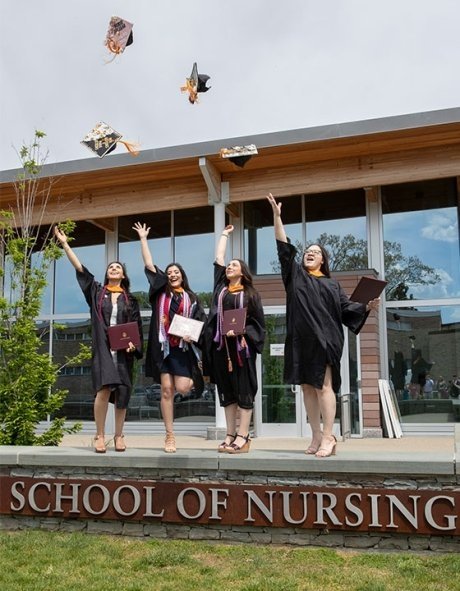 Nursing students, in front of the school of nursing, dressing in caps and gowns, throwing their caps in the air