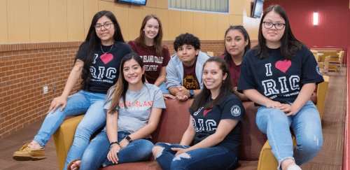 Group of students wearing RIC tee shirts happy in a residence hall 