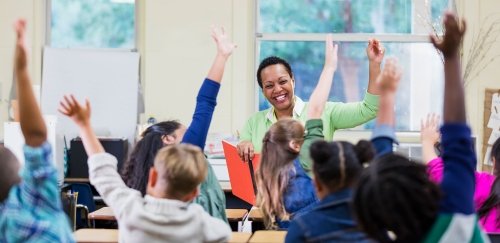 Teacher with kids at desks, energetically raising their hands