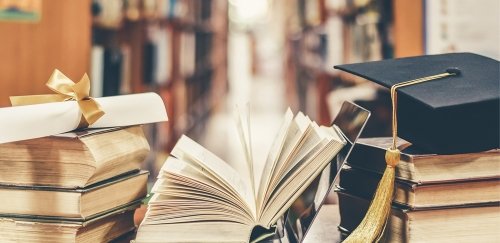 books, mortar board and diploma in library