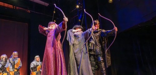 Theatre students on stage, in costumes, with bows and arrows