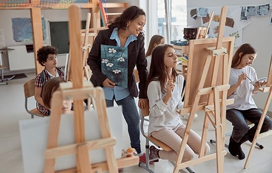 Art teacher instructing students as they paint at easels