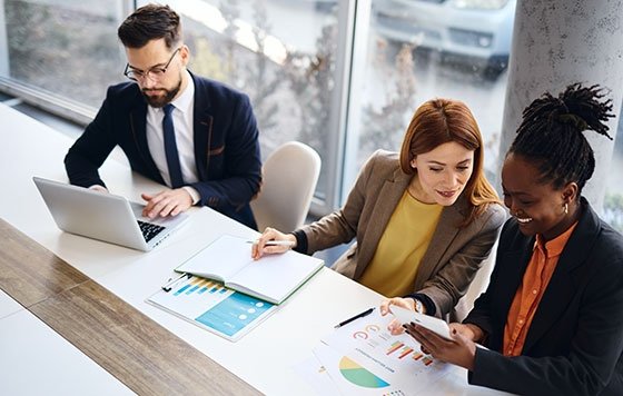 Three people working in office with laptop, tablet, charts, notebook