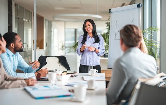 Woman leading a meeting, drawing a chart with others listening at table