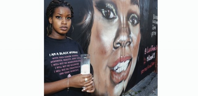 RIC student activist Brooxana Pierre stands in front of a Breonna Taylor mural holding a candle