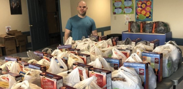 RIC alumnus Felix Colon stands behind a table full of food packages for families in need