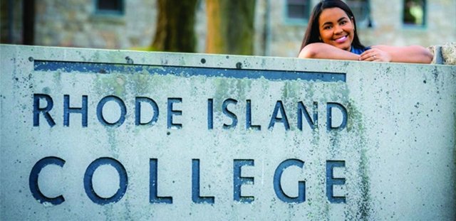 RIC graduate Ruth Feliz-Lima stands behind a Rhode Island College sign