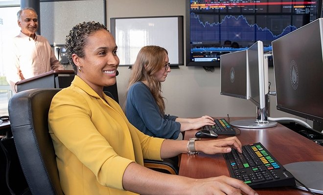 Two students in finance lab with professor in background