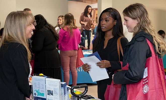 Two students talking to an employer at the health and education job fair