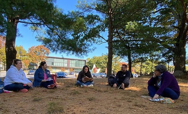 People sitting under trees on campus, sharing their writing