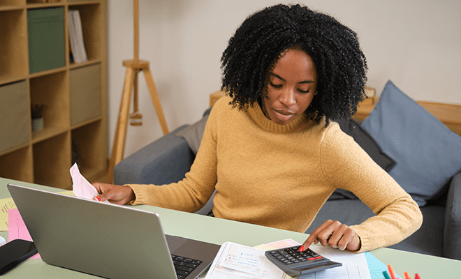 Female, black accountant working with invoices, calculator, and laptop