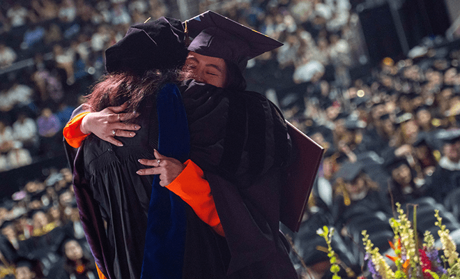 Graduate being embraced by faculty member