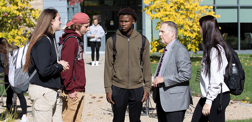 President Warner talking to a small group of students outside, on campus