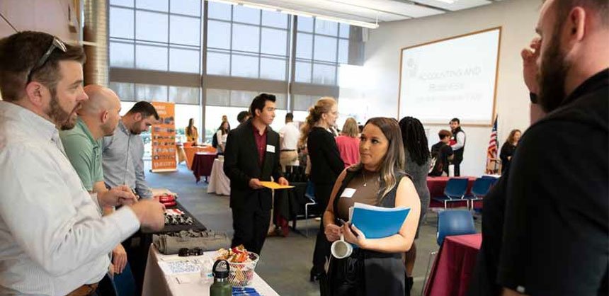 Female student holding folder at job fair speaking with prospective employer