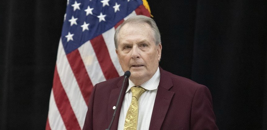 President Jack R. Warner speaking on stage with flag behind him